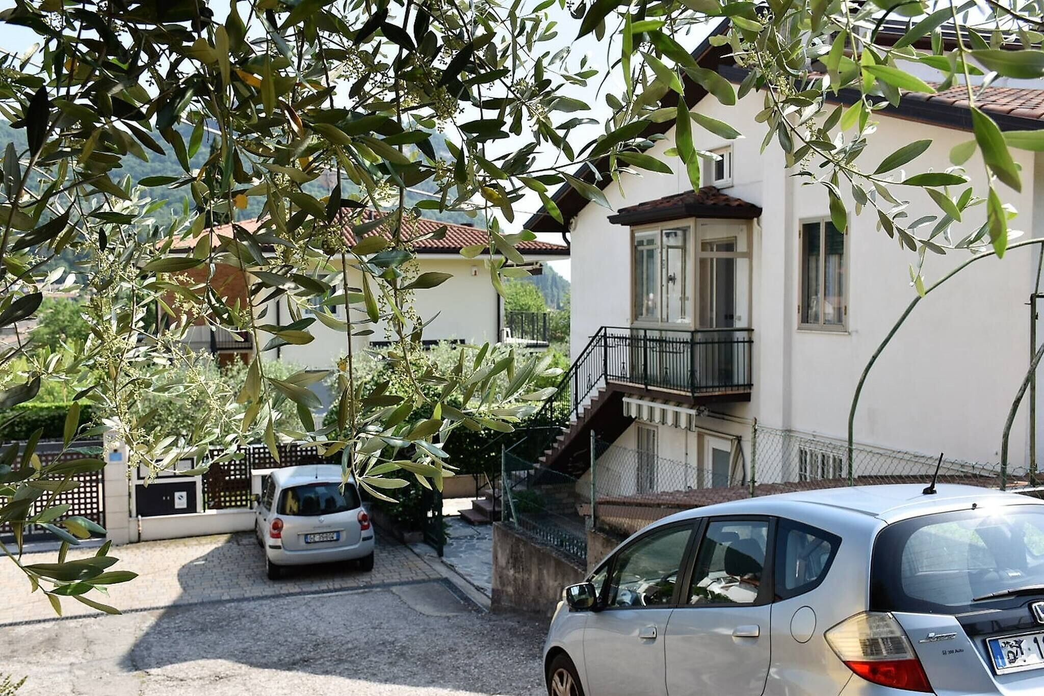 A residential area with a white building, a staircase leading to a balcony, and two parked cars.