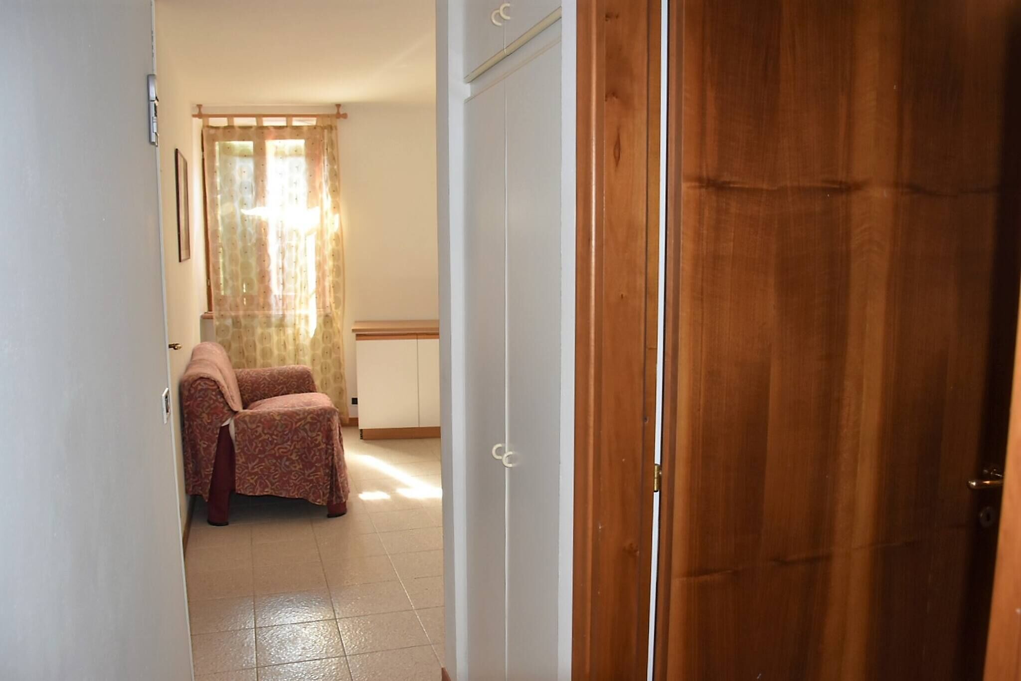 Un couloir avec une porte en bois, une chaise à motifs et une armoire blanche.
