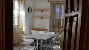 Ein Essbereich mit einem weißen Tisch und Stühlen, einer Uhr an der Wand und Vorhängen an den Fenstern.