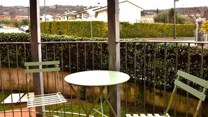 Un balcó amb una taula, dues cadires, una taronja i vista cap a cases al fons.