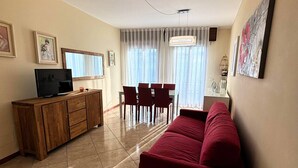 Una sala de estar con un sofá rojo, un mueble de madera, un televisor y un comedor con sillas y una mesa.
