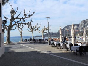 An outdoor café with tables and chairs, a view of the sea, and bare trees. - Catullo House in Garda (Garda)