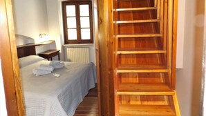 A bedroom with a wooden staircase, a bed with a white duvet, a nightstand, a window, and a radiator. - Catullo House in Garda (Garda)