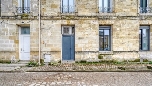 Un bâtiment en pierre avec une porte bleue, une porte blanche et une fenêtre ornée d’une grille métallique.