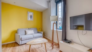 Un salon moderne avec un canapé gris, une table basse en bois, un lampadaire et un téléviseur fixé au mur.