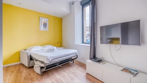 Une chambre à coucher avec un lit, une télévision, une fenêtre et un plancher en bois.