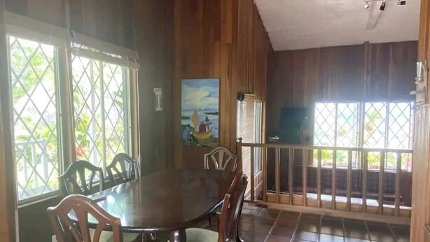 Uma área de refeições com mesa redonda e cadeiras, paredes de madeira e janelas amplas com vista para o verde.