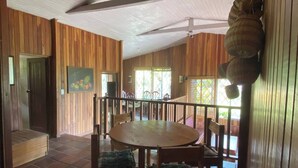 Interior de madeira com uma mesa de jantar redonda e cadeiras, uma escada e um ventilador de teto.