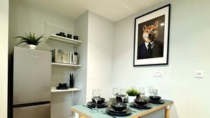 Una cocina moderna con refrigerador integrado, banco de madera y una mesa de comedor preparada para cuatro personas, con platos negros y copas de vino.
