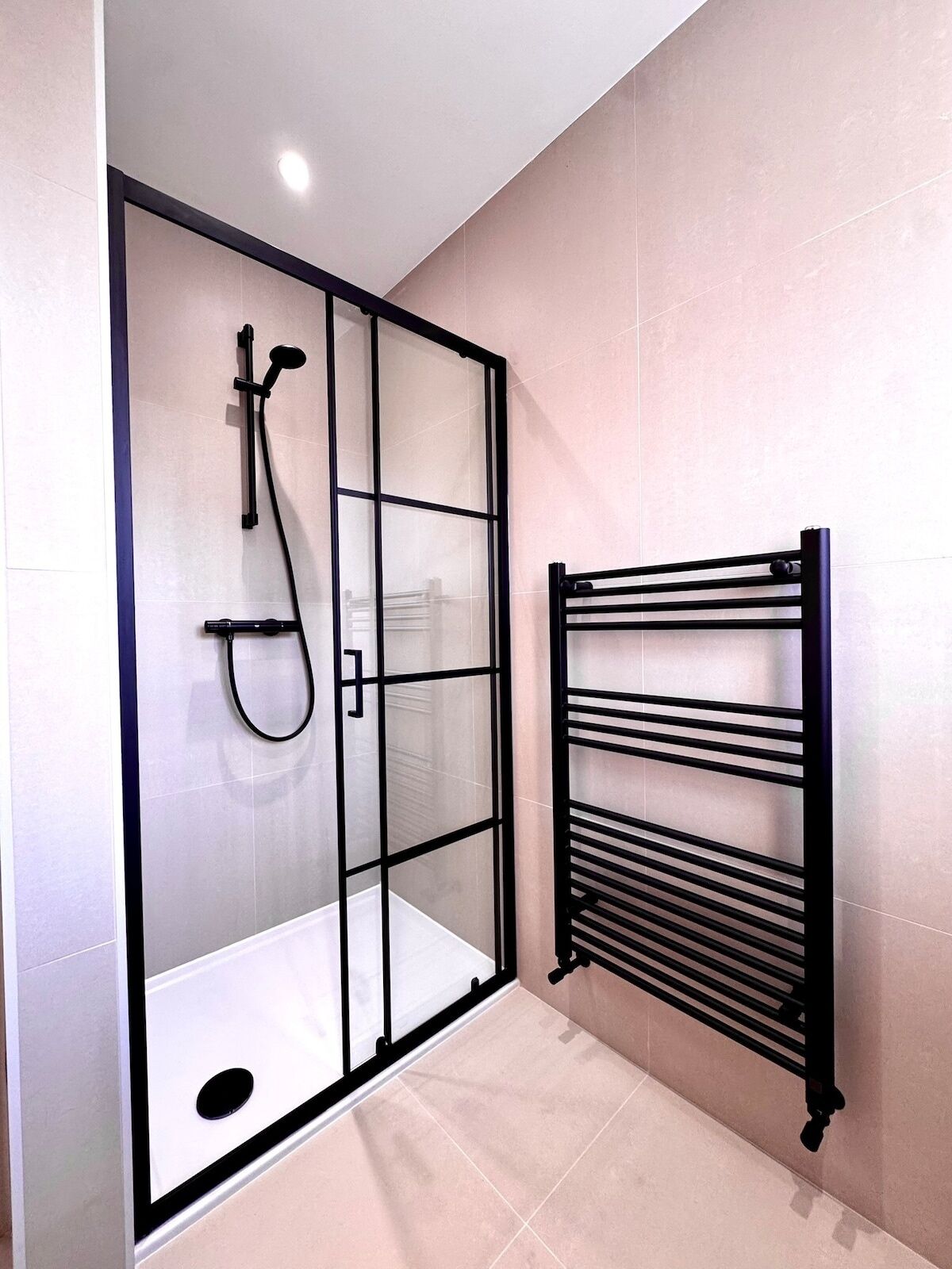 Ein modernes Badezimmer mit Duschkabine aus Glas, einem schwarzen Handtuchhalter und Fliesenboden.