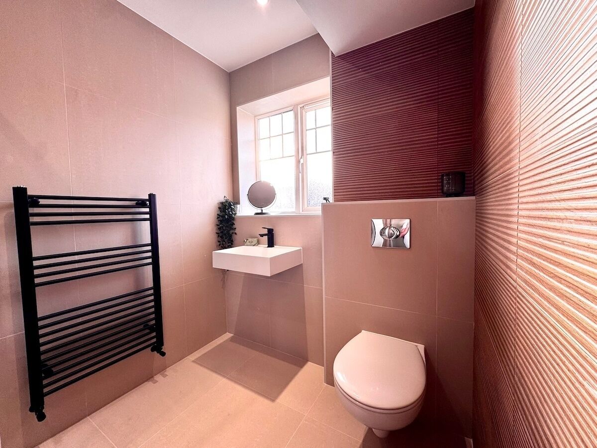 A bathroom with a black towel rack, a white sink, a mirror, and a toilet.