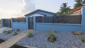 A modern building with a blue exterior, a gated entrance, and a gravel pathway with plants.