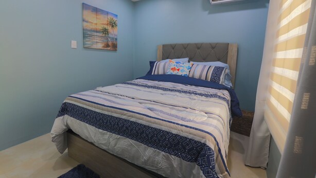 A bedroom with a bed, a painting, an air conditioner, and a curtain.