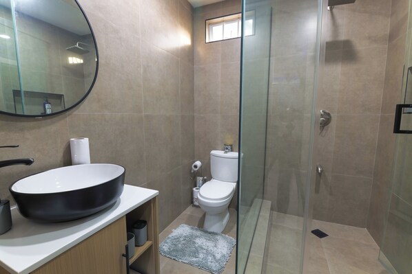 A bathroom with a round black sink, a toilet, and a glass shower enclosure.