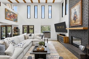 A modern living room with a sectional sofa, a fireplace, a flat-screen TV, and a large window with multiple panes. - Luxe Chapel Retreat |Chapel Views|Swim Spa | Sauna (Sedona)
