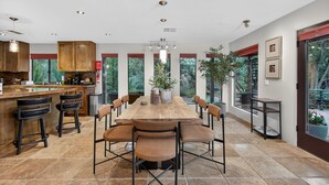 A modern kitchen with a large dining table, bar stools, and a view of the outdoors through large windows. - Luxe Chapel Retreat |Chapel Views|Swim Spa | Sauna (Sedona)