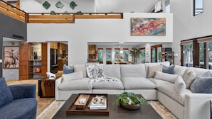 A spacious living room with a large sectional sofa, a coffee table, and a dining area with a high ceiling and exposed beams. - Luxe Chapel Retreat |Chapel Views|Swim Spa | Sauna (Sedona)