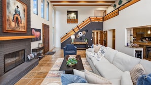 A spacious living area with a fireplace, a staircase, and a kitchen visible in the background. - Luxe Chapel Retreat |Chapel Views|Swim Spa | Sauna (Sedona)