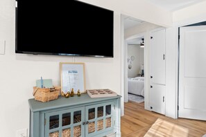 A room with a TV mounted on the wall, a framed certificate, a blue cabinet with storage, and a door leading to another room.