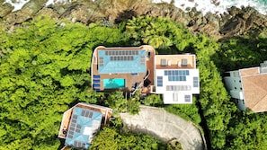 An aerial view of a resort with a swimming pool, a separate building with a solar panel roof, and lush greenery surrounding the property. - The Breeze Villa, newest ocean front boutique oasis (St Thomas)