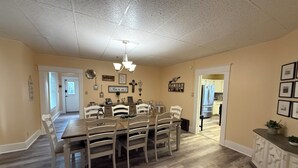 A dining area with a wooden table and chairs, a chandelier, and a kitchen visible through an open door. - Historic District Home with Proud N.M.M.I. Family Legacy (Roswell)