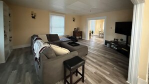 A spacious living room with a large sectional sofa, a flat-screen TV, and a dining area in the background. - Historic District Home with Proud N.M.M.I. Family Legacy (Roswell)