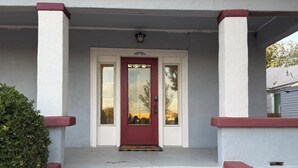A house with a red door, white exterior walls, and a small porch with steps leading to the entrance. - Historic District Home with Proud N.M.M.I. Family Legacy (Roswell)