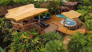 A tropical outdoor area with a pool, wooden tables, and chairs. - Hummingbird Villa (La Fortuna)