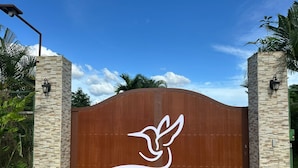 A gated entrance with a stylized bird logo, flanked by stone pillars and a curved metal gate. - Hummingbird Villa (La Fortuna)