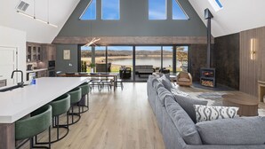 A spacious interior with a high ceiling, a large dining area, a cozy seating area, and a view of the outdoors. - AFrame at Beaver Lake |Hot Tub. Epic Patio & Views (Rogers)