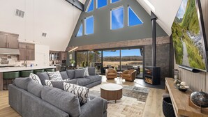 A spacious living area with a large gray sectional sofa, a round coffee table, and a fireplace. - AFrame at Beaver Lake |Hot Tub. Epic Patio & Views (Rogers)