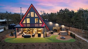 A modern house with a triangular roof, large windows, and a patio area with outdoor furniture. - AFrame at Beaver Lake |Hot Tub. Epic Patio & Views (Rogers)