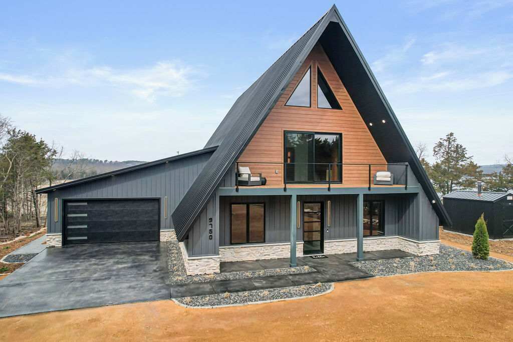 Une maison moderne de forme triangulaire, dotée d’un garage, d’un porche couvert et de fondations en pierre.