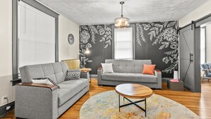 Uma sala de estar moderna com dois sofás cinzas, uma mesa de centro de madeira e um tapete colorido.