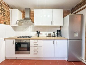 Une cuisine avec des meubles blancs, un réfrigérateur en acier inoxydable, une cuisinière à gaz et un grille-pain.