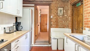 A compact kitchen with white cabinets, a wooden countertop, and a brick wall. - New | Cosy & Stylish City Centre Home | Sleeps 6 (Canterbury)