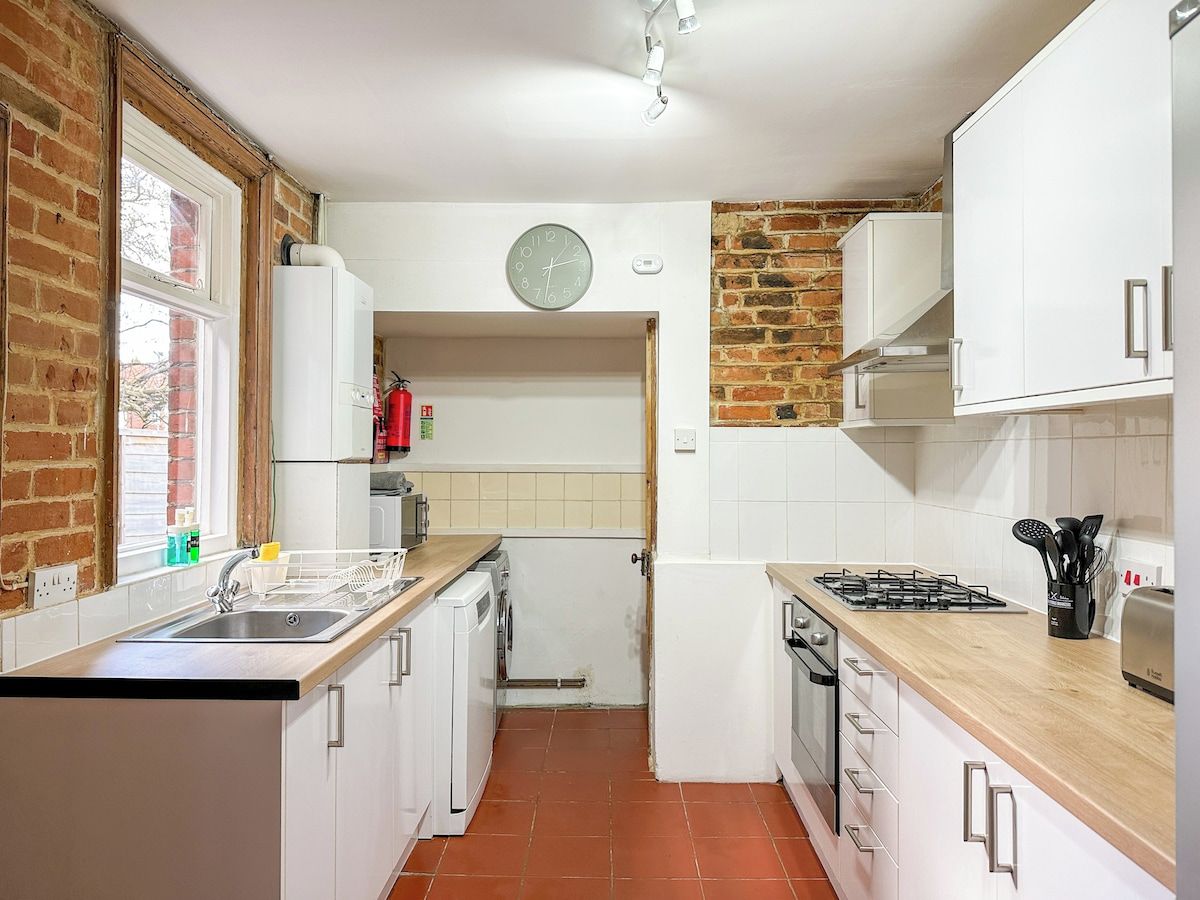 A kitchen with white cabinets, a brick wall, a window, a clock, and a stove.