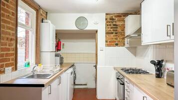A kitchen with white cabinets, a brick wall, a window, a clock, and a stove.
