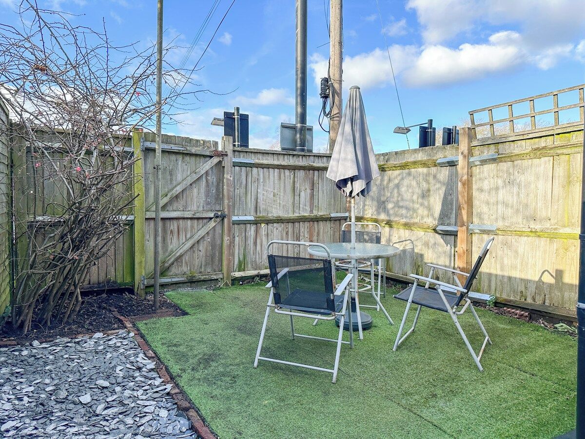 A fenced backyard with artificial grass, a metal table and chairs, and a covered umbrella.