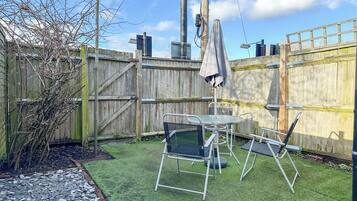 A fenced backyard with artificial grass, a metal table and chairs, and a covered umbrella.