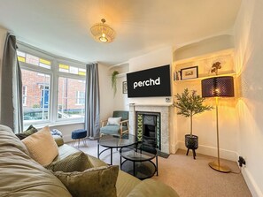 A living room with a sofa, a glass table, a fireplace, a TV, and a floor lamp.
