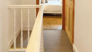 A bedroom with a bed, a wooden door, and a white railing. - New | Cosy & Stylish City Centre Home | Sleeps 6 (Canterbury)
