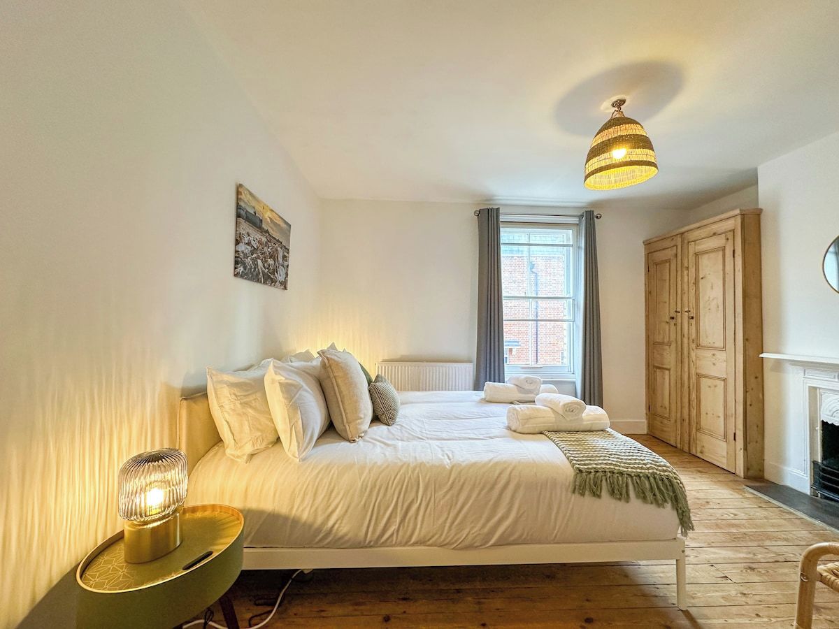 A bedroom with a bed, bedside table, lamp, window, and a wardrobe.