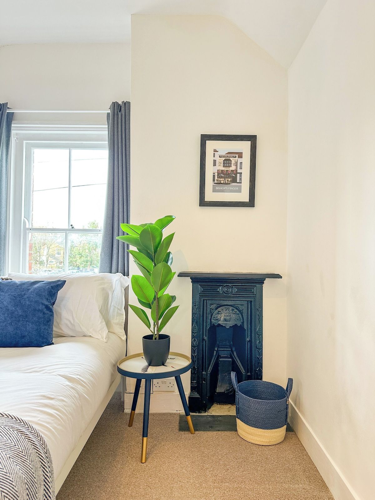 A bedroom with a bed, a potted plant, a fireplace, and a framed picture on the wall.