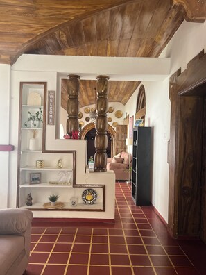 Une pièce avec un plafond en bois, une console centrale dotée d’étagères, un canapé et un sol carrelé.