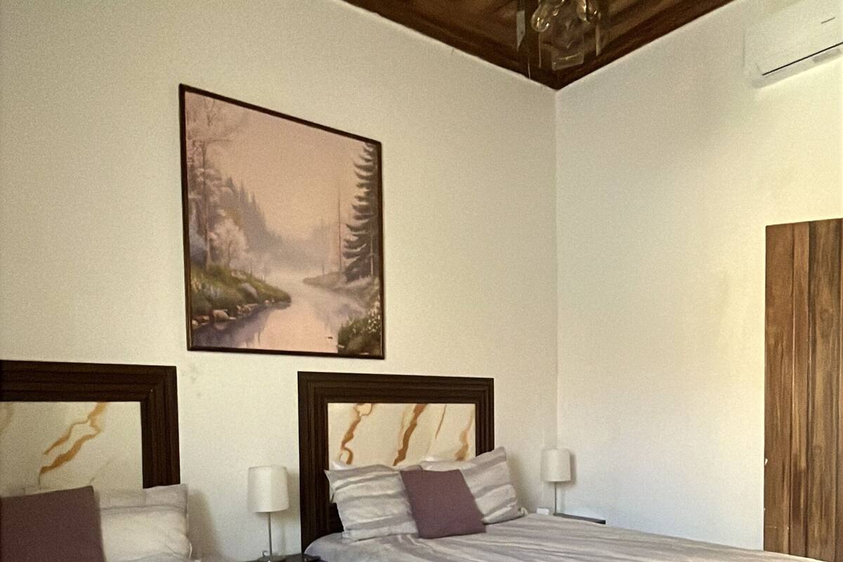 A hotel room with two beds, a painting on the wall, and a wooden ceiling.