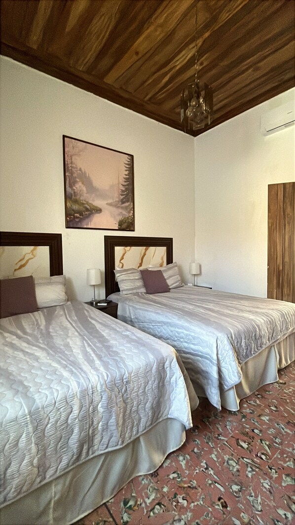 Une chambre d’hôtel avec deux lits, un tableau au mur et un plafond en bois.