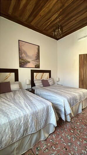 A hotel room with two beds, a painting on the wall, and a wooden ceiling. - Club 27 Hostal Cafe & Spa (Santa Ana)