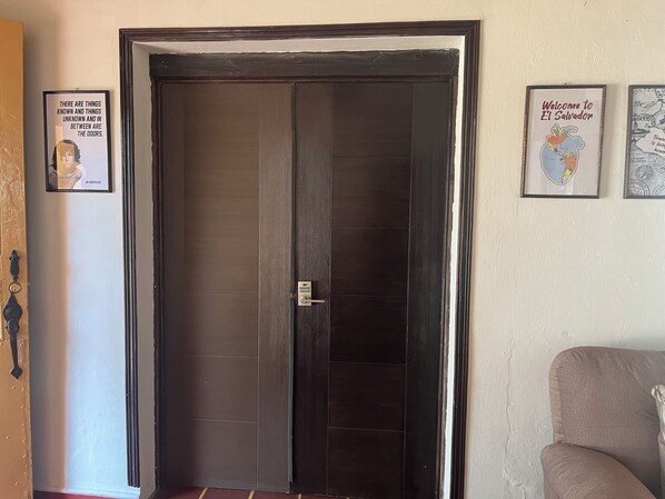 A dark wooden door with a keypad lock, a framed quote on the wall, and a framed welcome sign. - Club 27  Hostal Cafe & Spa (Santa Ana)