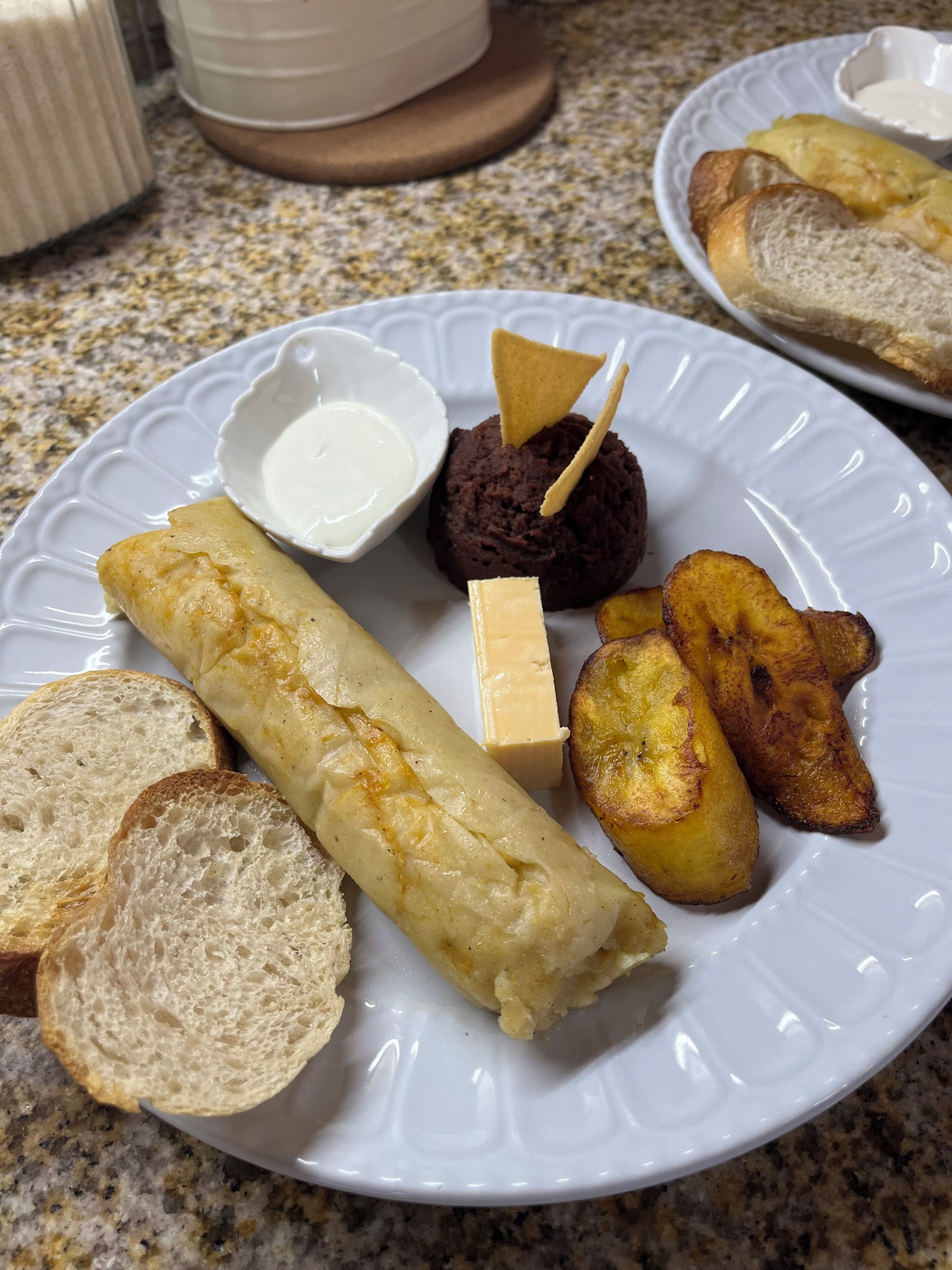 Un plat amb una pasta, un bol petit de crema, un dolç de xocolata, un tros de formatge i plàtans fregits.